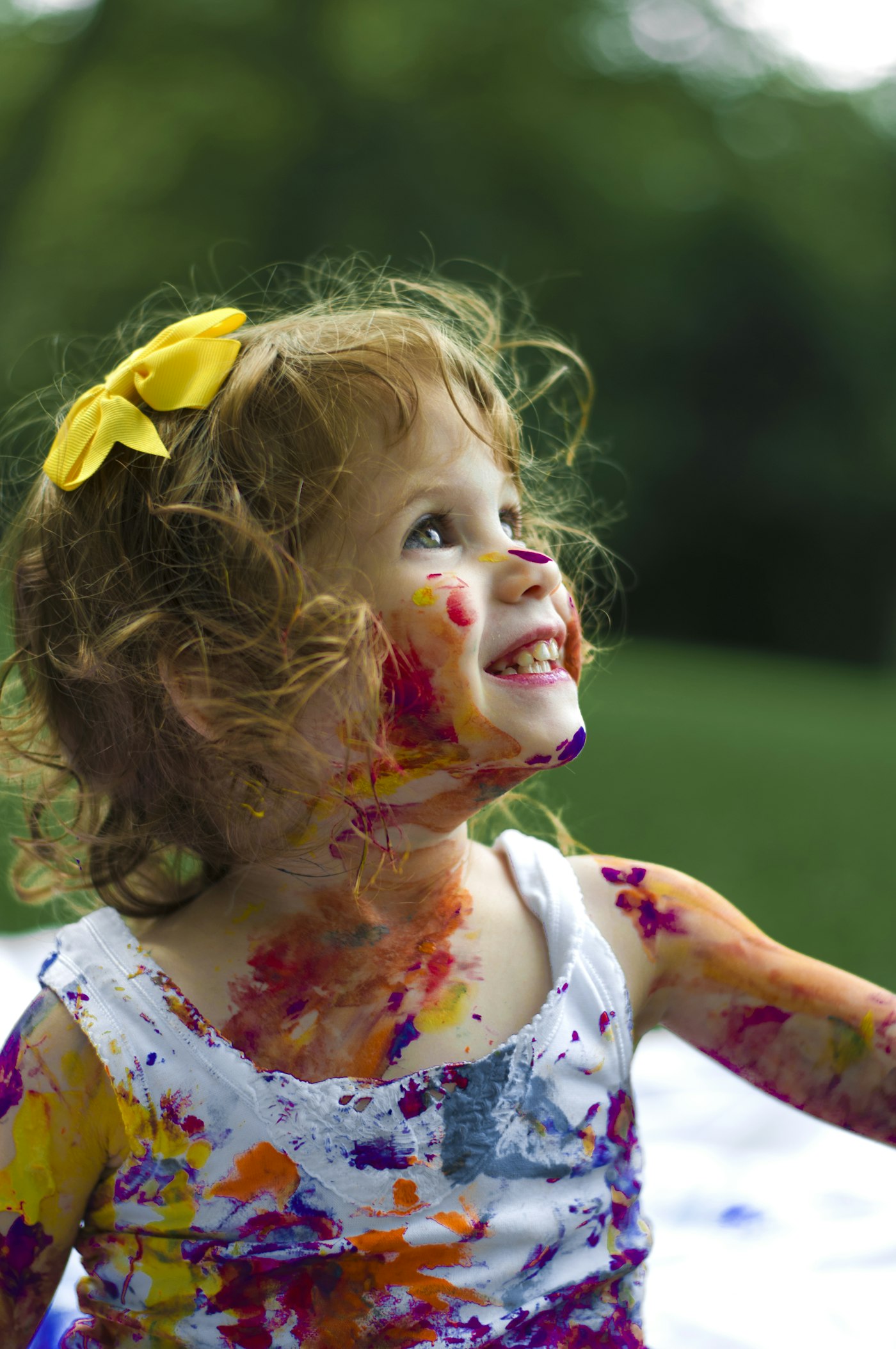 A smiling child covered in colourful paint after a creative session